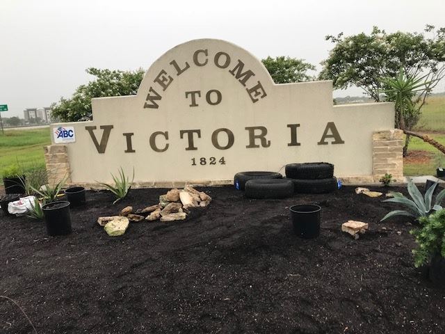 Welcome to Victoria sign with old tires in plant bed