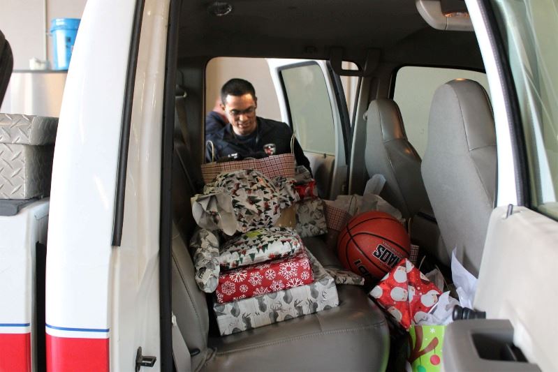 Man places gift bag in truck backseat alongside stacked gift boxes, bags and a basketball.