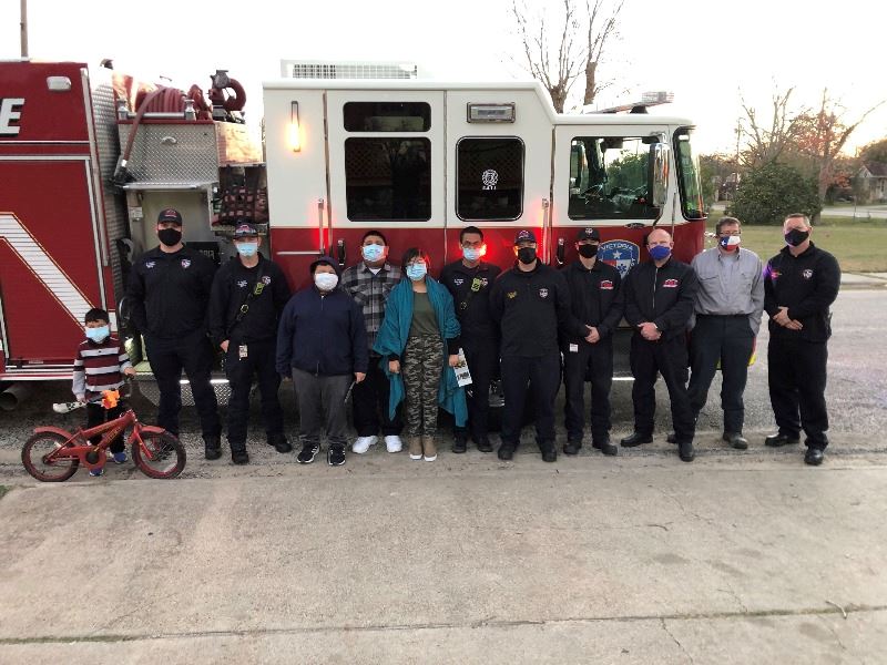 Firefighters and residents, including a young boy with a bike, pose in front of a fire engine.