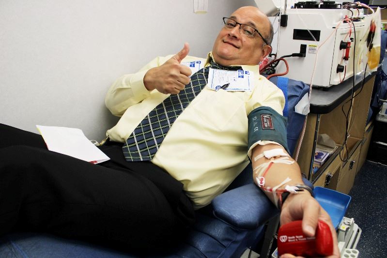 Man is hooked up to blood donation unit. He gives a thumbs-up.