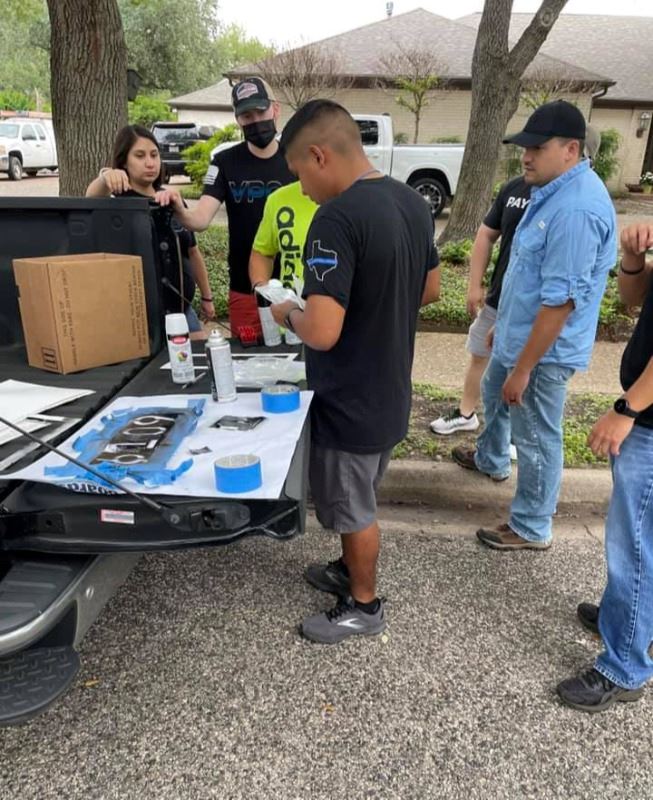 People gather around an open pickup bed and arrange number stencils