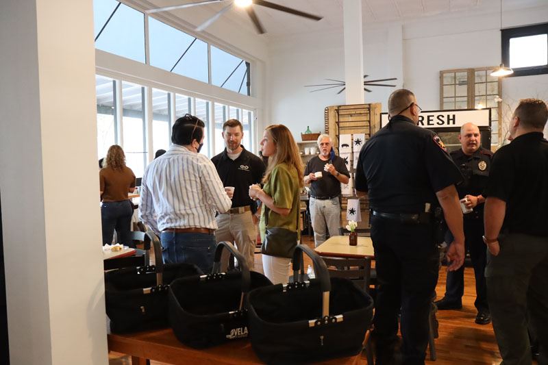 People mill about, some holding coffee, indoors at Vela Farms.