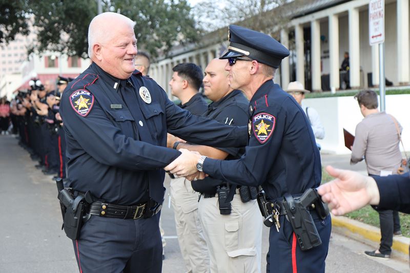 A police officer shakes the hand of an officer standing in a row of applauding officers.