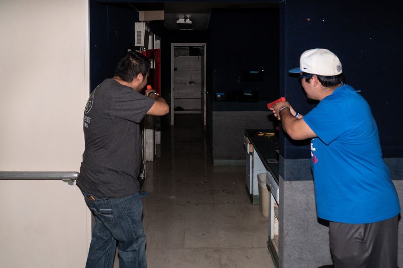 Two people aim plastic weapons into a dark room