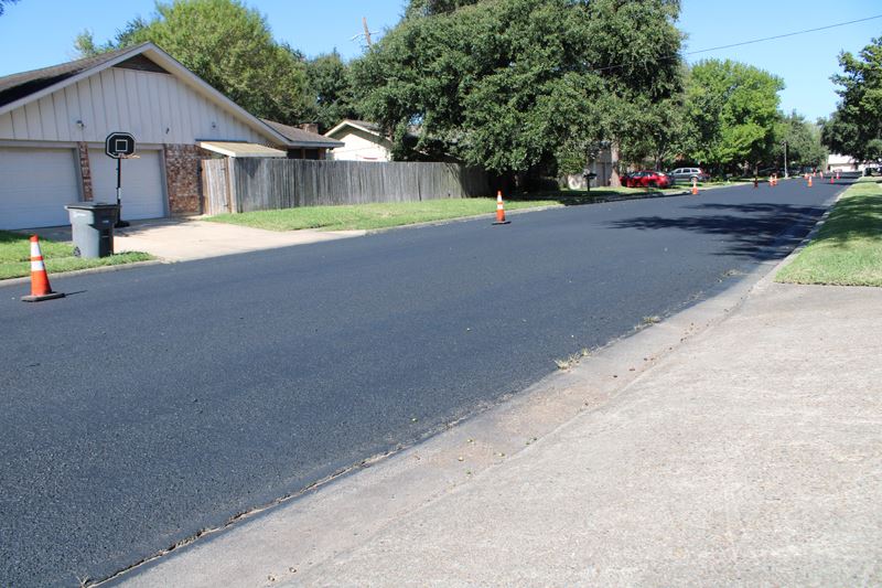 A dark black neighborhood street. Sparsely placed traffic cones line the side of the road.