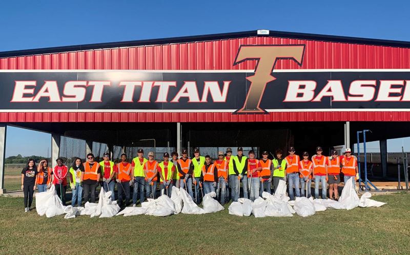 High school students pose with collected trash bags in front of East Titan Baseball facility