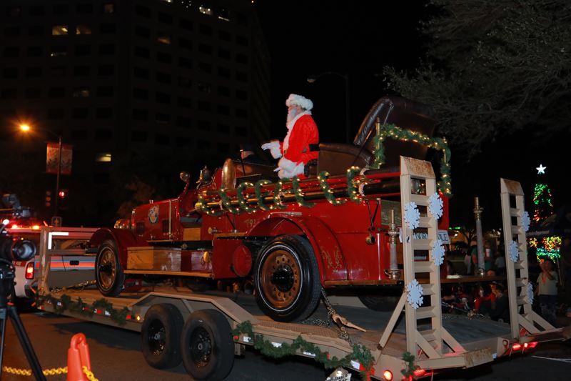 Santa Claus waves from an old-fashioned fire truck mounted on a trailer.